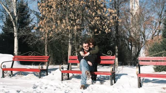 成熟的夫妇坐在冬季公园的长凳上