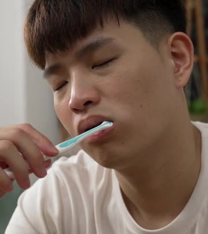 垂直屏幕: 穿着t恤的疲倦的亚洲人早上在家里的卧室里刷牙时从打瞌睡中醒来。