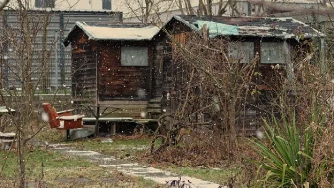 社会最贫穷的部分。一座古老的木屋，位于飘落的大雪中的现代建筑中。老年人的贫困。旧木制小屋。温暖的午后