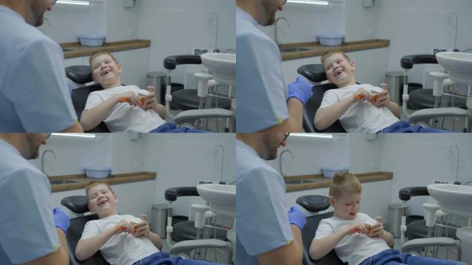 男牙医向男孩和他的母亲展示了如何以嬉戏的方式正确刷牙的下巴模型。孩子坐在牙科椅上拍手。慢动作