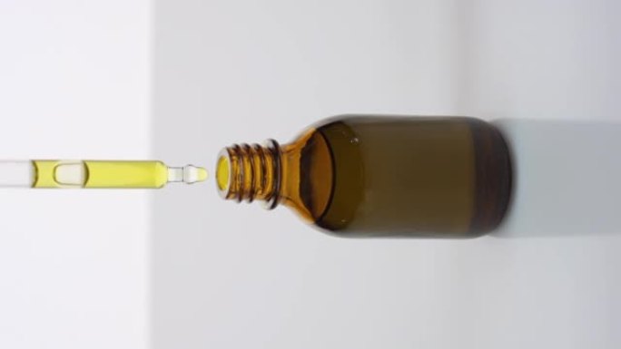 滴管将黄色的油滴入灰色背景的棕色瓶子中