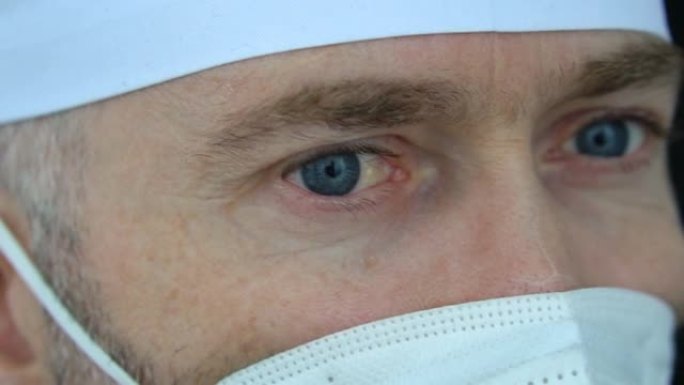 疲倦严重的成熟男性专业医生在口罩，眼镜和防护套件中服用大量患者后，由于冠状病毒的流行