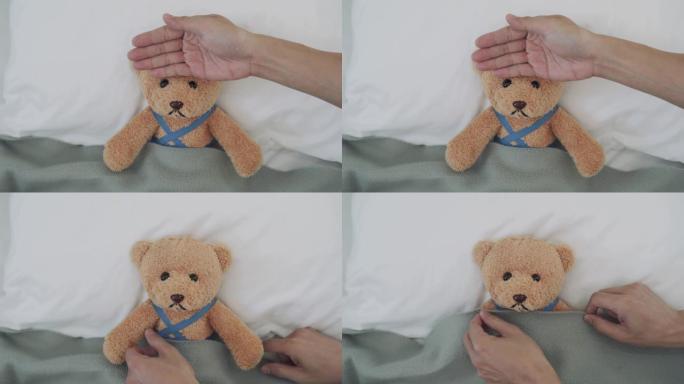 感觉生病和发烧的概念。用熊作为孩子的代表。男子用手测量头部温度，发现发高烧感觉凉爽，因此请用毯子为身