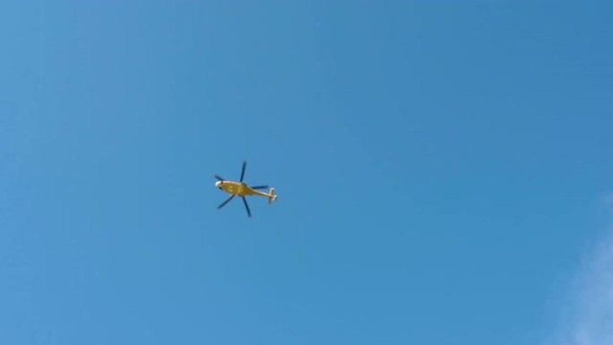 仰视拍摄在晴朗的蓝天背景下飞行的黄色直升机，紧急救援直升机，空中救护车，军事空军或空中服务的消防员