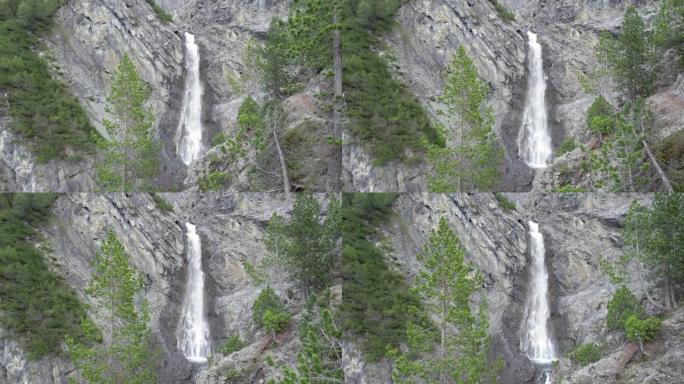 空中无人机的镜头缓慢地穿过树冠，飞向一个引人注目的瀑布，因为它在瑞士的一个陡峭的山崖边缘上瀑布。