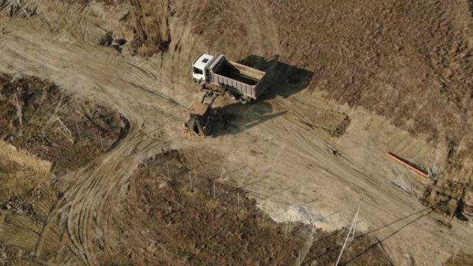 一辆拖拉机的鸟瞰图，它将土壤装载到卡车的后部。道路施工。秋天