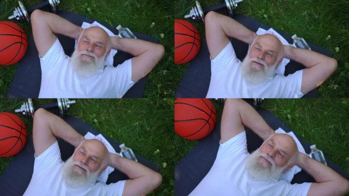 现场摄像机在体贴的老人周围旋转，看着远处的梦想躺在夏日公园的运动垫上。自信的白人男性退休人员喜欢在户