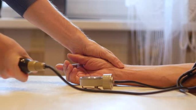 测量老年人的血压是一个话题。成年儿子在家中用眼压计为年迈的父亲测量脉搏和血压。关爱老年亲属的健康。