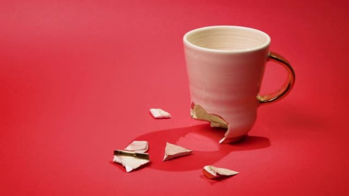 破碎的茶杯孤立在红色背景上。破裂的咖啡杯和易碎的陶瓷片