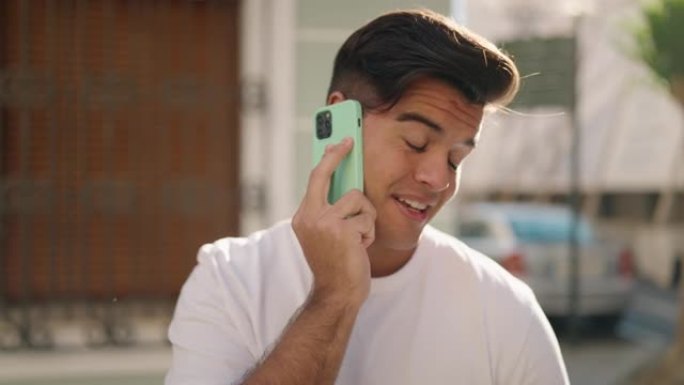 年轻的西班牙裔男子微笑着自信地在街上的智能手机上交谈