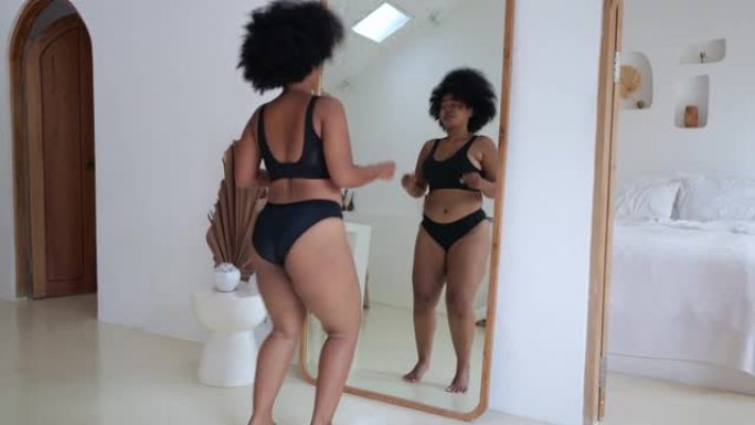 一位女性大码模特穿着黑色内衣在镜子前跳舞。女人不注意多余的体重，她爱自己。身体积极的概念。