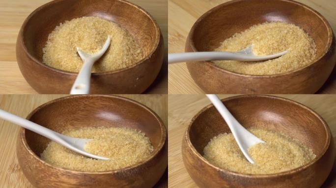 木碗中的蔗糖，勺子在木板上旋转。碗中旋转的红糖。甜美健康