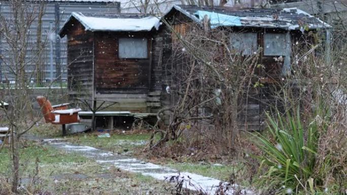 社会最贫穷的部分。一座古老的木屋，位于飘落的大雪中的现代建筑中。老年人的贫困。旧木制小屋。凉爽的晨光
