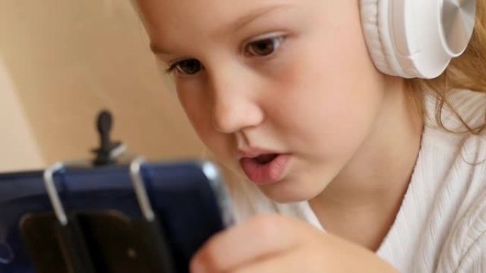 一个可爱的十几岁的女孩正在使用电话并戴着耳机进行视频通话。在线教育基础和附加。使用互联网进行远程学习