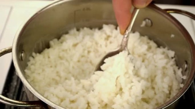 用厨房勺子在金属锅里煮圆米饭。