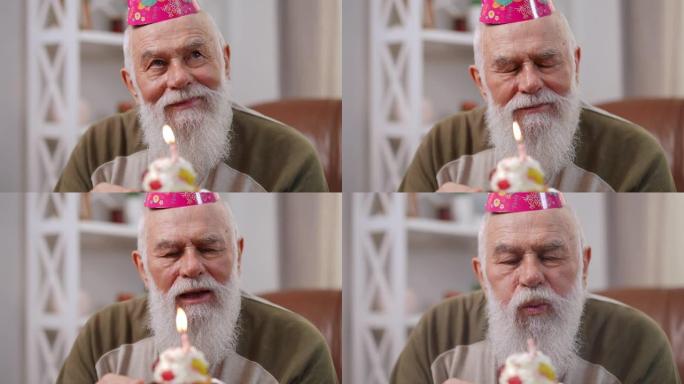 特写微笑满意的大胡子老人想着闭上眼睛在生日那天许愿，在纸杯蛋糕上吹出燃烧的蜡烛。快乐的老高加索退休人