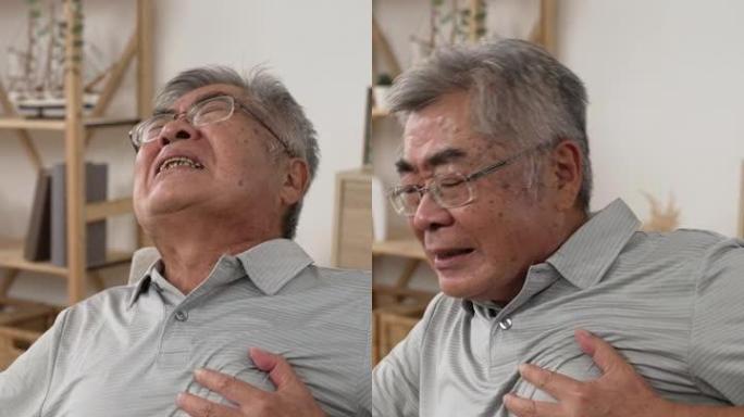 竖屏: 不安分的资深亚韩男子坐在家里客厅沙发上摸胸口喊叫。戴眼镜坐在沙发上的悲伤疲惫时尚老男性。