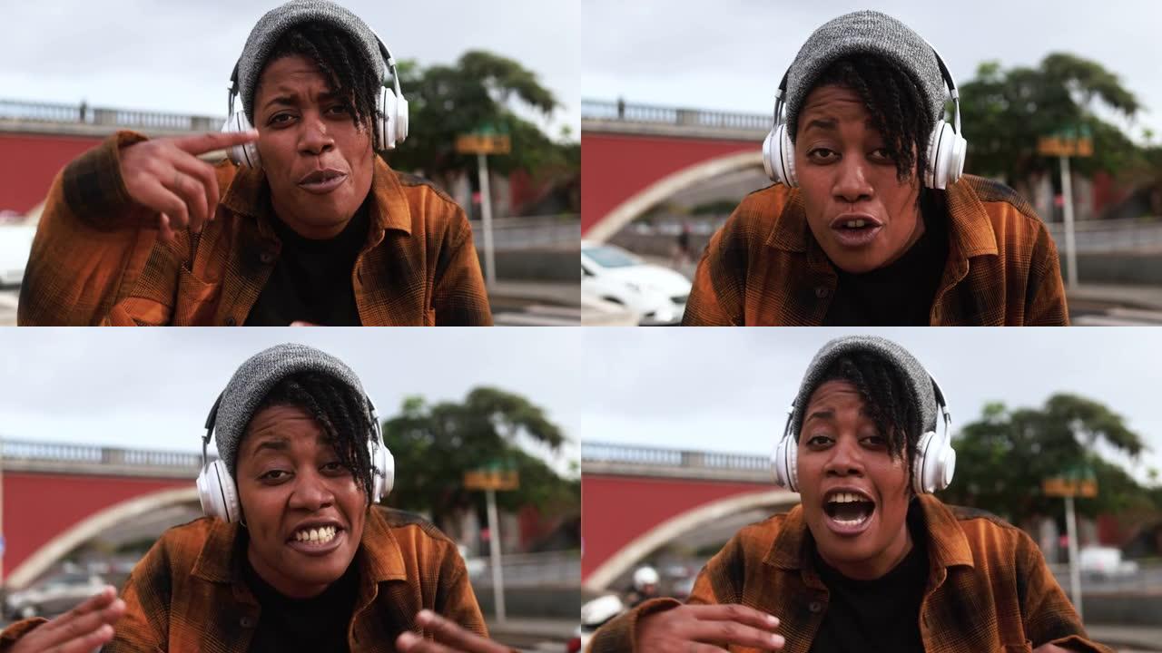 非洲裔美国妇女在城市街道背景中戴着无线耳机说唱一首歌 -- 地下生活方式概念