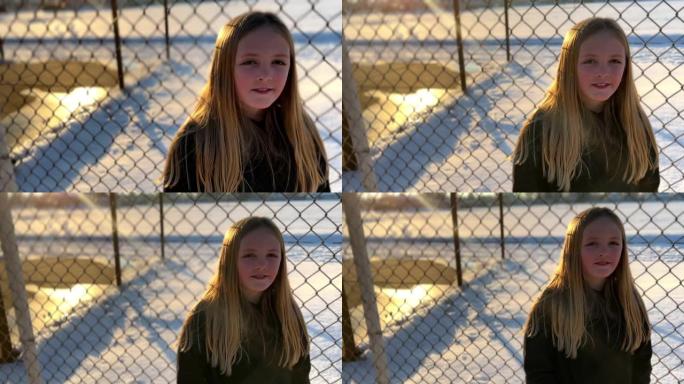 一所小学附近的铁丝网围栏上的一个年轻漂亮女孩的肖像