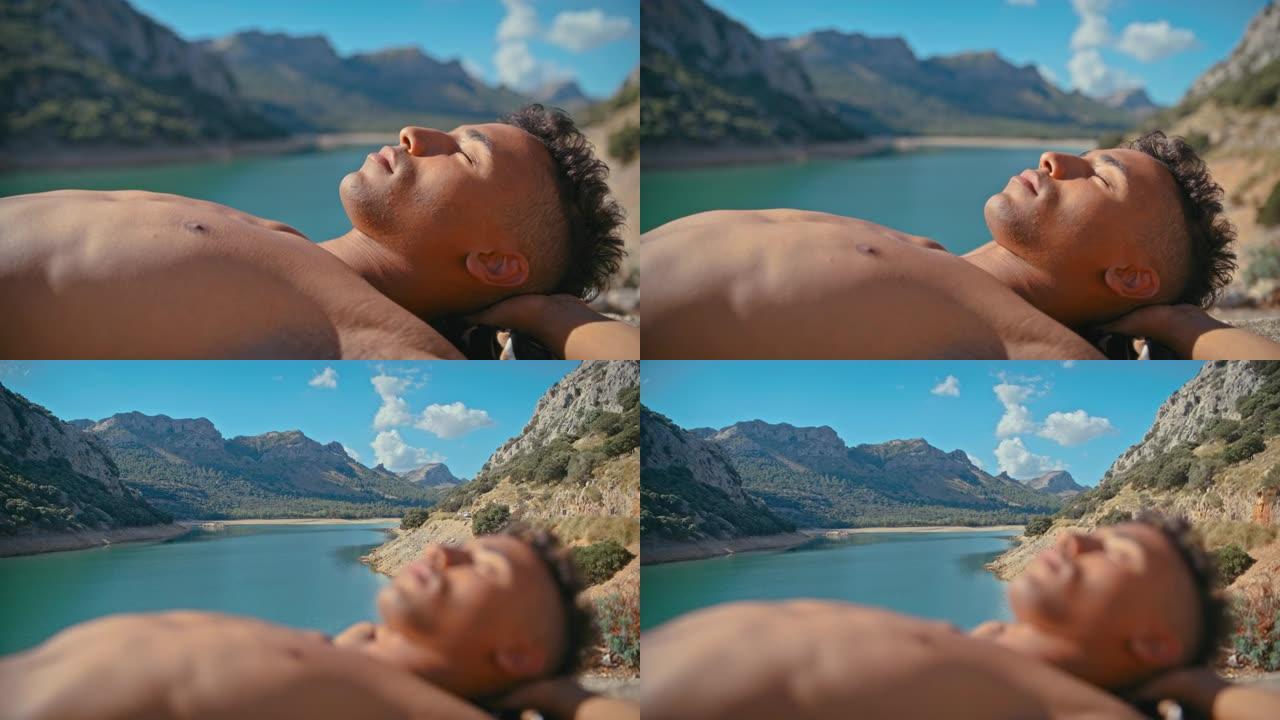 特写的年轻人躺在绿松石湖边的石头栅栏上晒日光浴