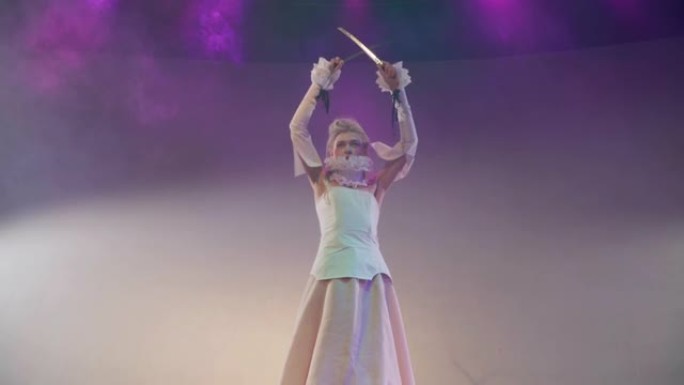 穿着白色优雅复古风格连衣裙的女演员在剧院舞台上模仿烟雾中的击剑。白人才女在聚光灯下的现代表演中扮演角