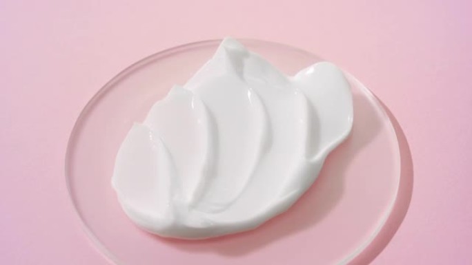 在淡粉色背景的圆形玻璃上拍摄白色奶油的起重机镜头