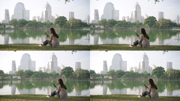 亚洲妇女很高兴通过早上在城市公园的电话在线聊天来放松身心，人们在城市自然环境中放松身心