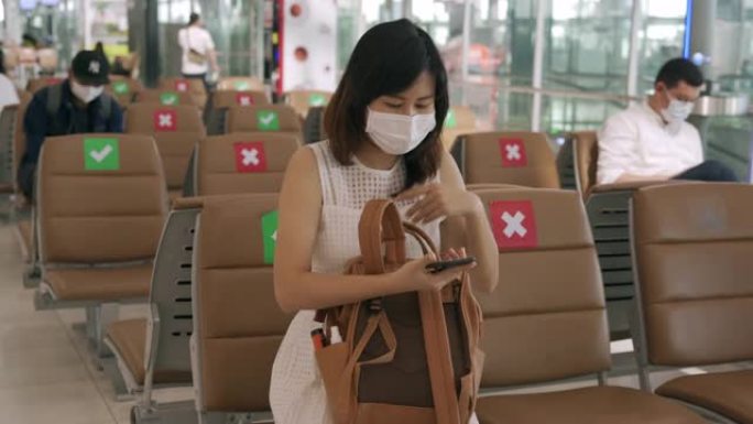 新常态概念。亚洲女性戴着口罩，坐在椅子之间，以减少冠状病毒的传播。在covid-19爆发期间，游客等