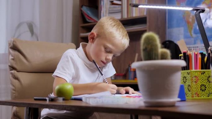 一个小孩子在家做作业，他坐在办公桌前，在笔记本上写字。