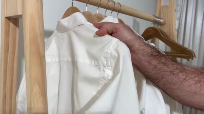 男士清洁白色衣橱只有男士毛茸茸的手是可见的，或者销售助理根据目的和尺寸在木制衣架上安排东西，用于文字