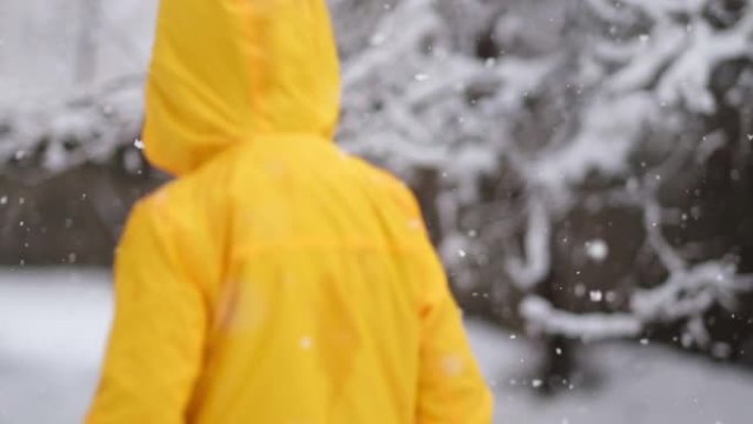 穿着黄色冬装的有趣小男孩在降雪时行走。孩子们的户外冬季活动。