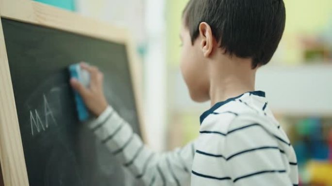 可爱的西班牙裔男孩学龄前学生在教室里擦黑板