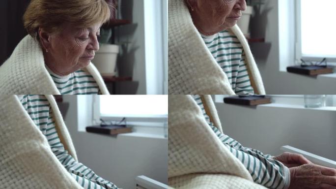 一位悲伤的老妇人肩上披着一件格子衣服，用电热器温暖她冰冷的双手。特写镜头从脸部移到手部