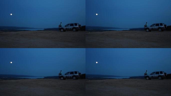 一个人独自坐在河边的汽车引擎盖上，在夜空下凝视着远方
