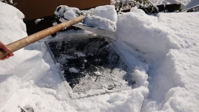 用铁锹清除房屋屋顶上的太阳能电池板上的冰雪