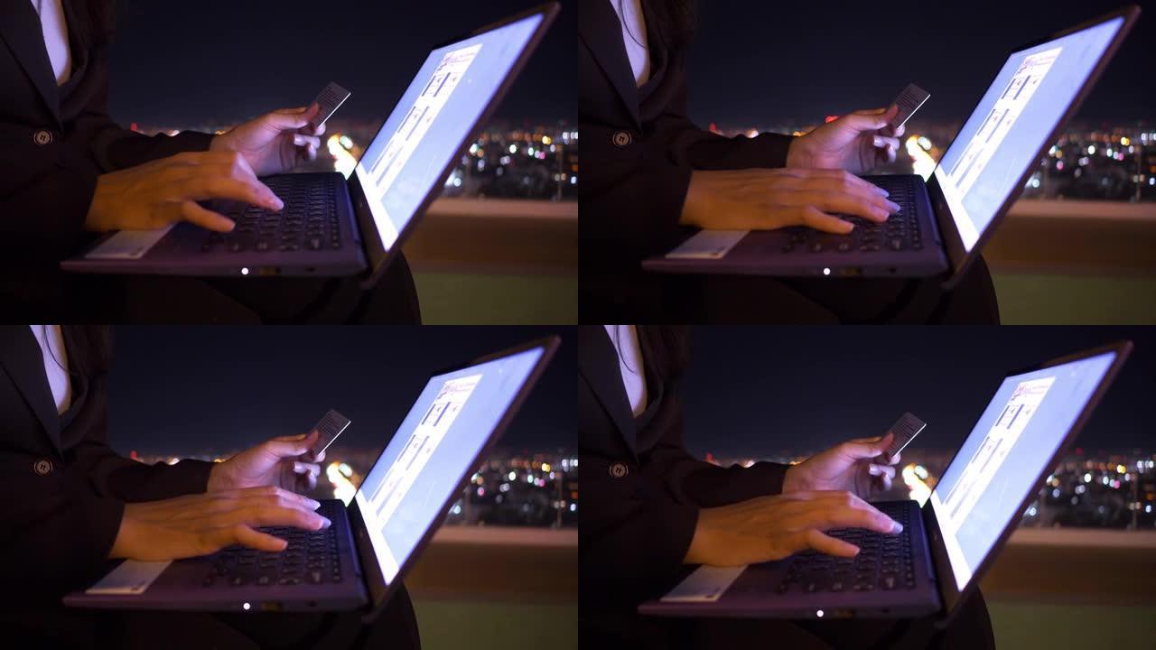 亚洲年轻女子的特写手正在用笔记本电脑上的信用卡在线购买。