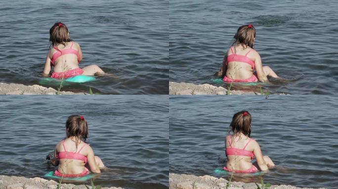 小女孩坐在海边向水中扔石头，慢动作