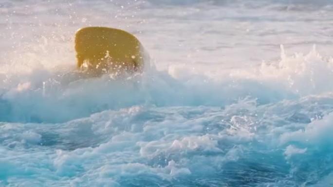 海浪喷出喷雾，露出爱斯基摩人用黄色冲浪板滚动后在水中冲浪的女人