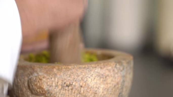 厨师拿起沉重的研钵和杵，准备将原始香料和草药的混合物转化为细磨的泰国绿咖喱酱。