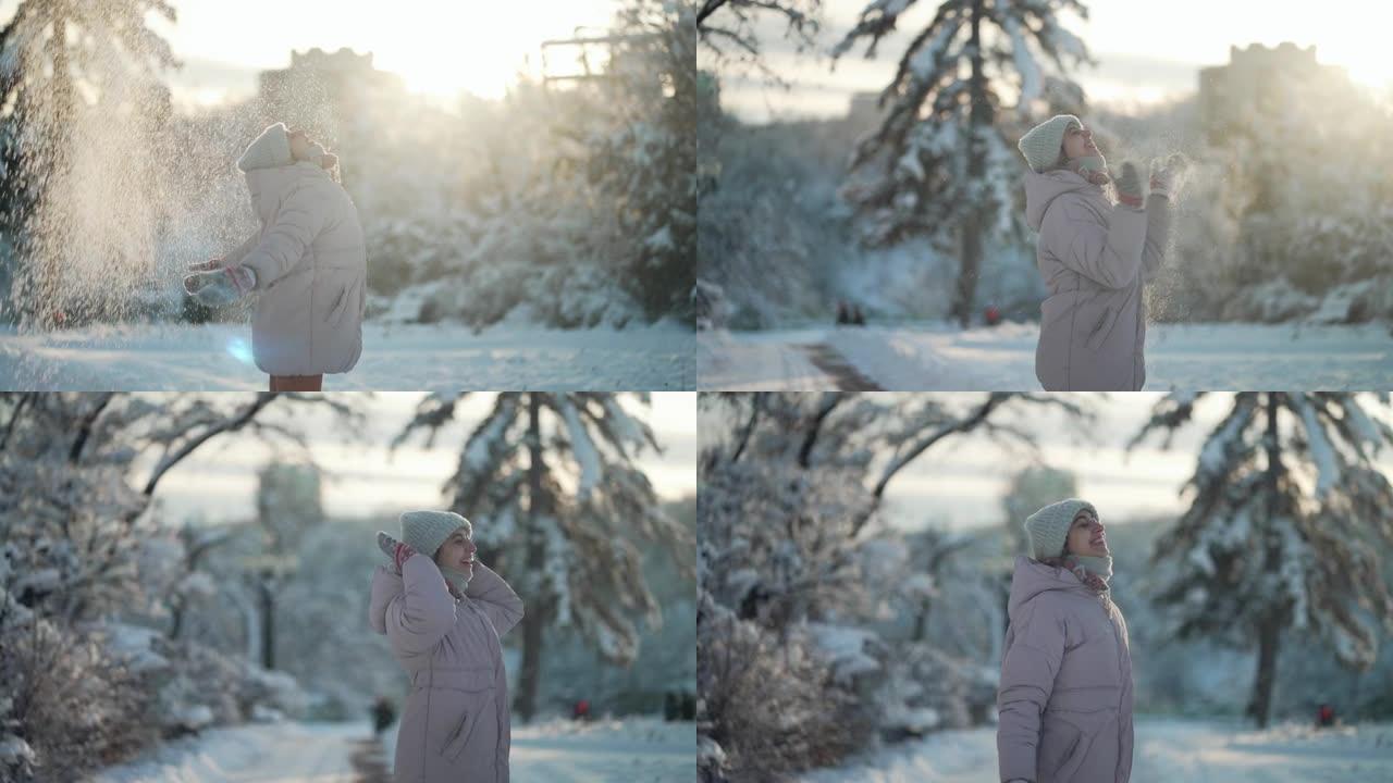 穿着暖和衣服的顽皮年轻女子在阳光明媚的冬季白雪皑皑的公园里撒雪，围着她转，用雪花拍手