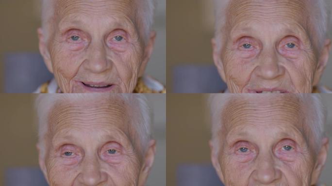 白人老妇看着相机的皱纹脸上的特写灰色眼睛。积极的女性高级退休人员坐在家里说话和微笑。幸福和衰老的概念