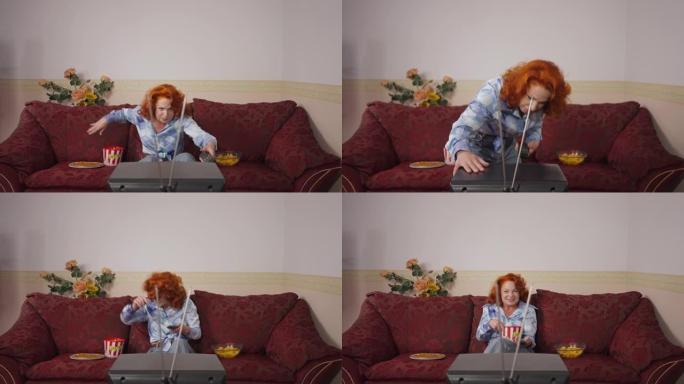 恼怒的复古女人用天线坐在沙发上看电影吃垃圾食品打老式电视。20世纪80年代20世纪70年代周末在家休