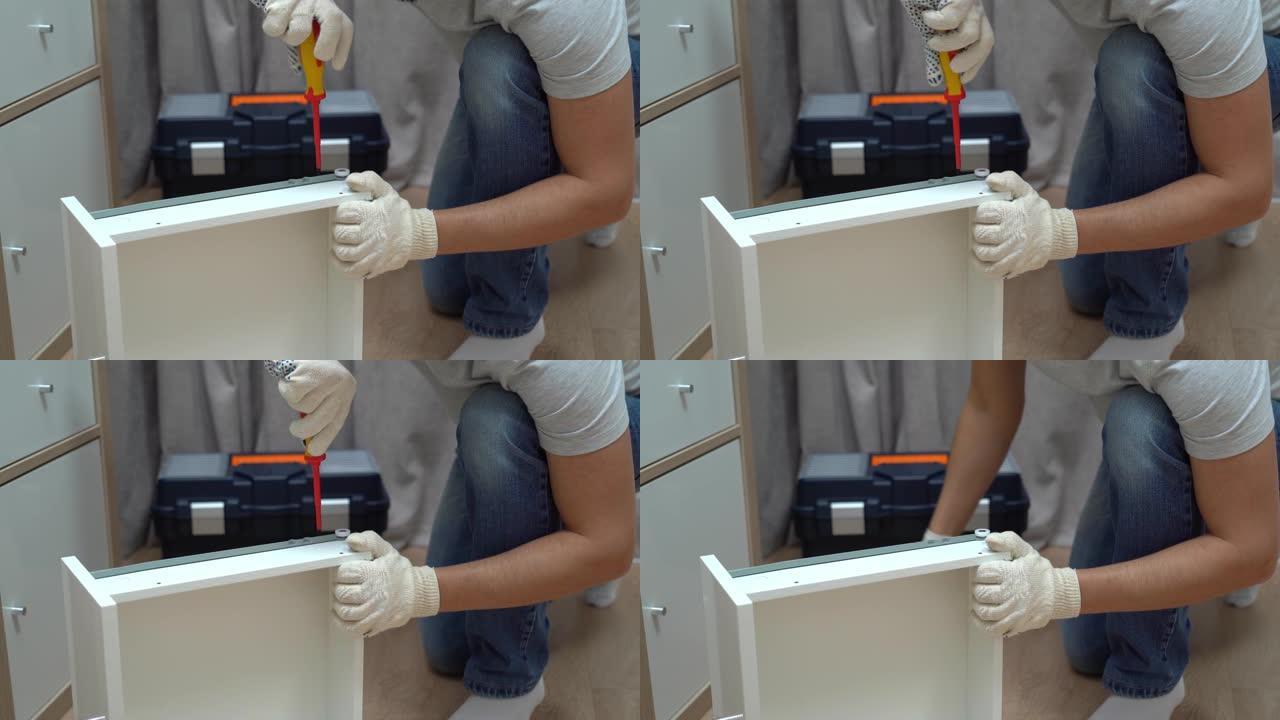 男人的手在木制衣柜和带工具的盒子的背景上使用螺丝刀组装抽屉。家具组装过程。