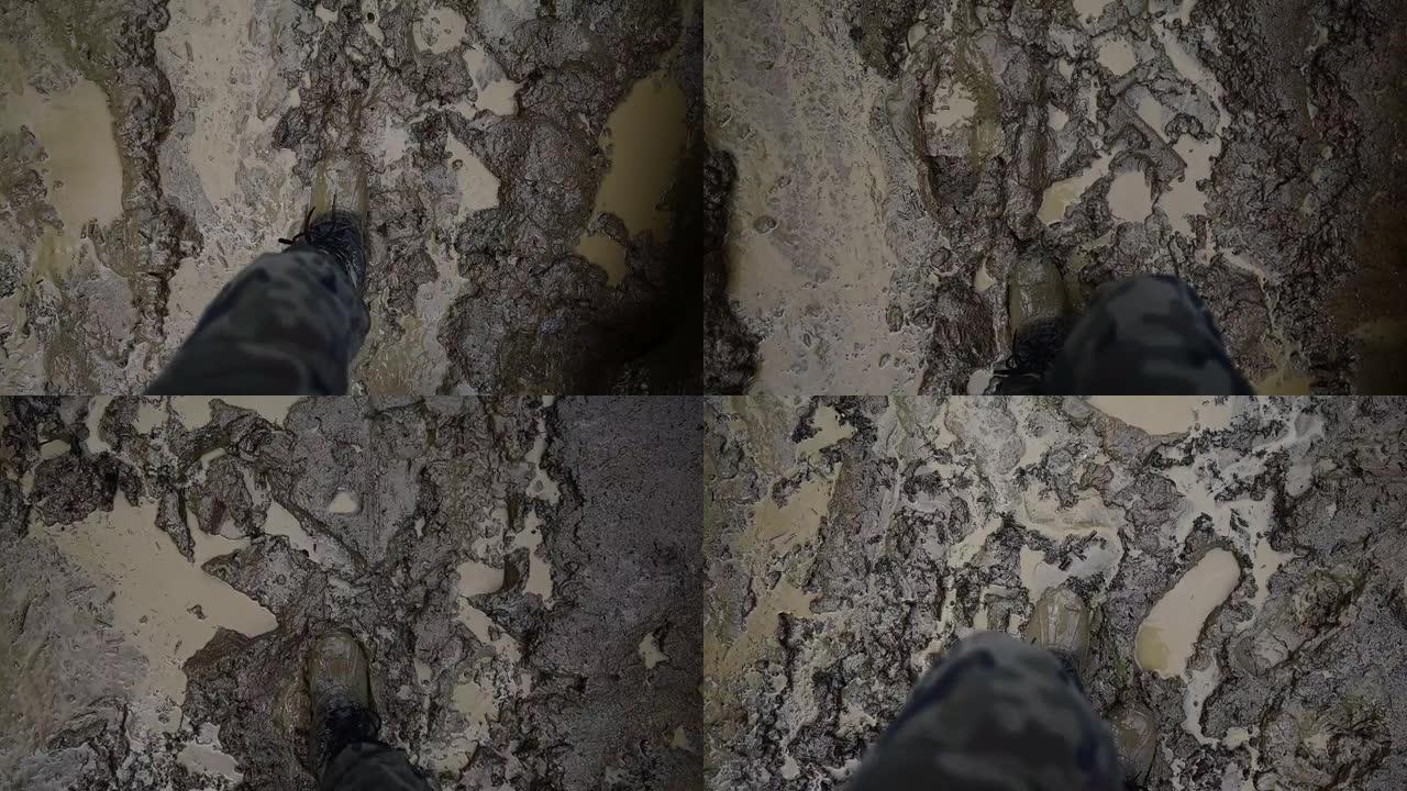 一个穿着军用迷彩服的男人的腿的特写，他的徒步胶靴在泥泞中很脏。