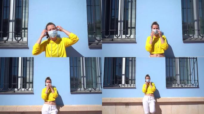 特写镜头放大了一个年轻的西班牙女孩戴上口罩靠在蓝色墙壁上的镜头