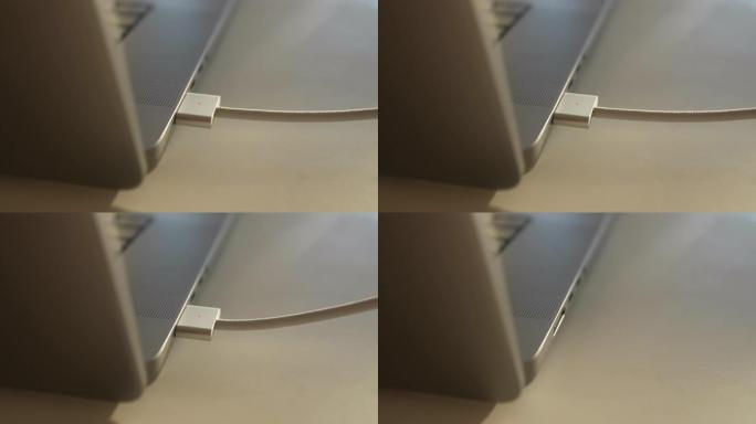 在阳光明媚的家庭办公室里，无法辨认的人从桌子上的笔记本电脑上断开磁性usb-c电源线的特写镜头。