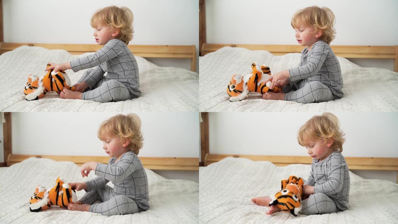 两岁的小男孩在舒适的房间里的床上和玩具老虎玩耍