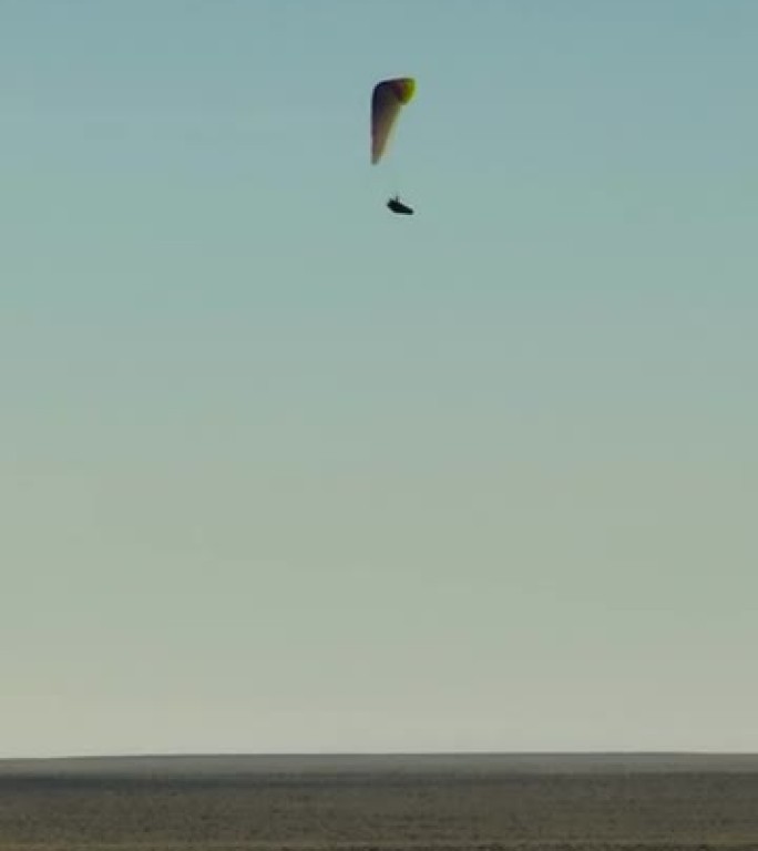 多色滑翔伞在大悬崖沙漠平原上空盘旋飞行