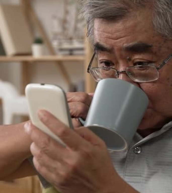 竖屏: 老人用手机看网络新闻，喝咖啡。老白发爷爷用手机享受一杯早茶。