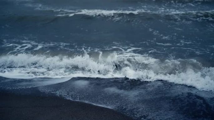 蓝色海潮席卷冰岛海滩。海浪泡沫撞击沙滩自然